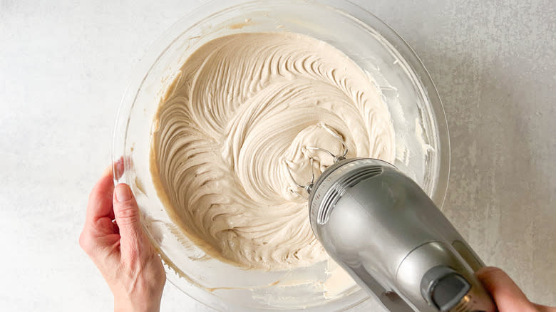 Whipping cinnamon-cashew frosting with hand mixer in mixing bowl