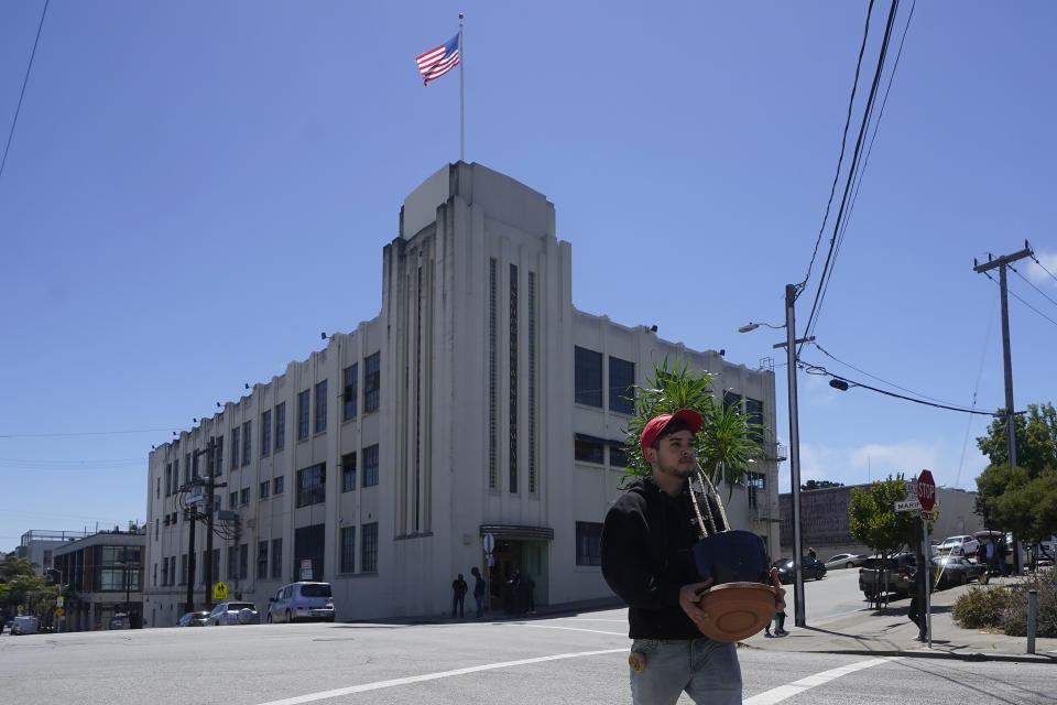 FILE - Anchor Brewing Co. employee Dimas Arellano carries his plants out of the company building, rear, to his car in San Francisco, Wednesday, July 12, 2023. A spokesman for Anchor Brewing says the company is open to a purchase offer from its employees but warned that time is running out. The 127-year-old San Francisco-based trailblazer of craft beers stunned beer lovers earlier in July when it announced it would cease operations. (AP Photo/Jeff Chiu, File)