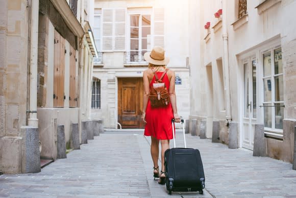 A traveling woman in a red dress with rolling luggage