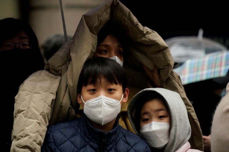 People wearing masks after the coronavirus outbreak wait in a line to buy masks as it rains in front of a department store in Seoul