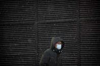 A man wearing a face mask to protect against the spread of the coronavirus walks along a street during a snowy morning in Beijing, Tuesday, Jan. 19, 2021. A Chinese province near Beijing grappling with a spike in coronavirus cases is reinstating tight restrictions on weddings, funerals and other family gatherings, threatening violators with criminal charges. (AP Photo/Mark Schiefelbein)