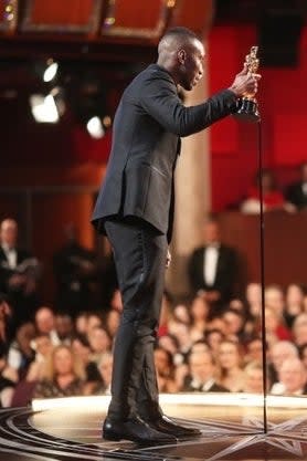 Mahershala on stage accepting award, audience in background, focus on joyous moment