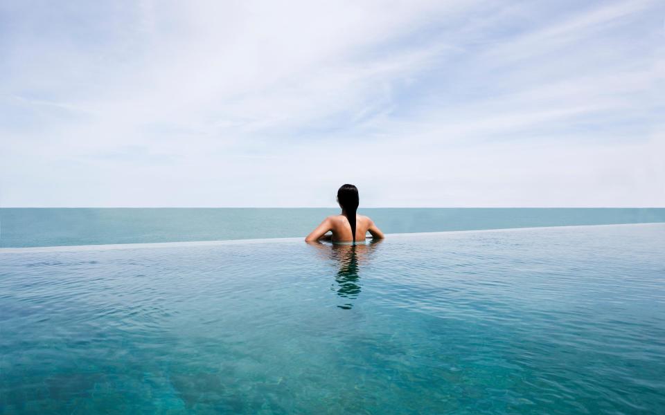 Woman on edge of infinity pool over sea - Angelo Cavalli/Getty