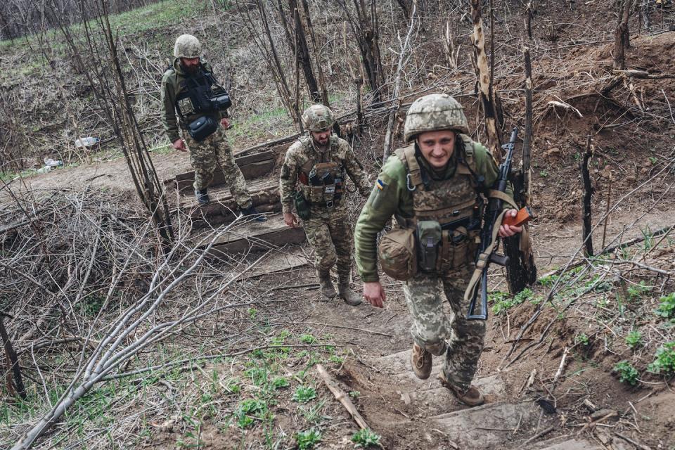 Three people in camouflage uniforms and helmets walk up a hill