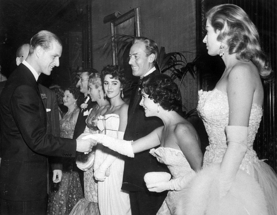 FILE - In this Nov. 23, 1955 file photo, Elizabeth Taylor curtsies as she is greeted by the Duke of Edinburgh at the premiere of "Cockleshell Heroes" at the Empire Theater in London. To the left of Elizabeth Taylor is her husband Michael Wilding and at his right is actress Jackie Lane. Buckingham Palace says Prince Philip, husband of Queen Elizabeth II, has died aged 99. (AP Photo/File)
