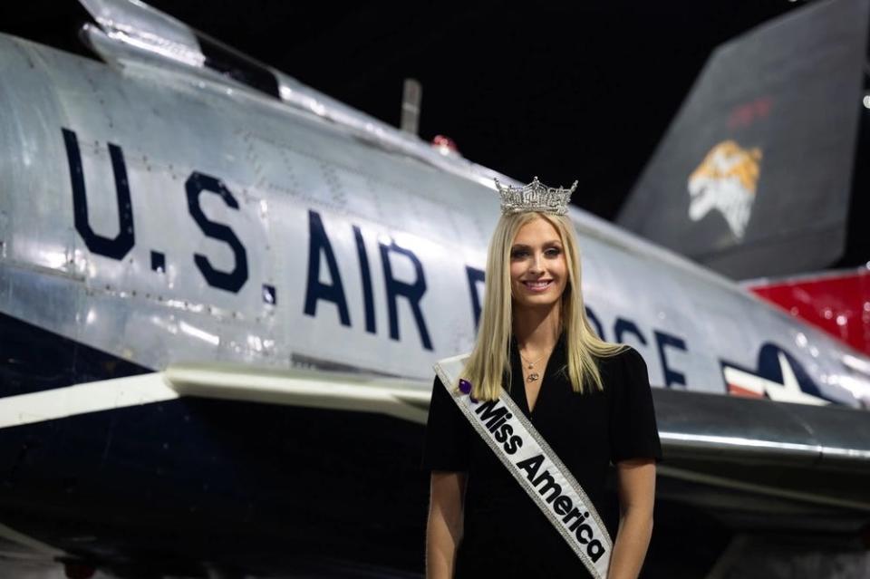 Madison Marsh, wearing her Miss America sash and crown, poses in front of an aircraft at the National Museum of the US Air Force.