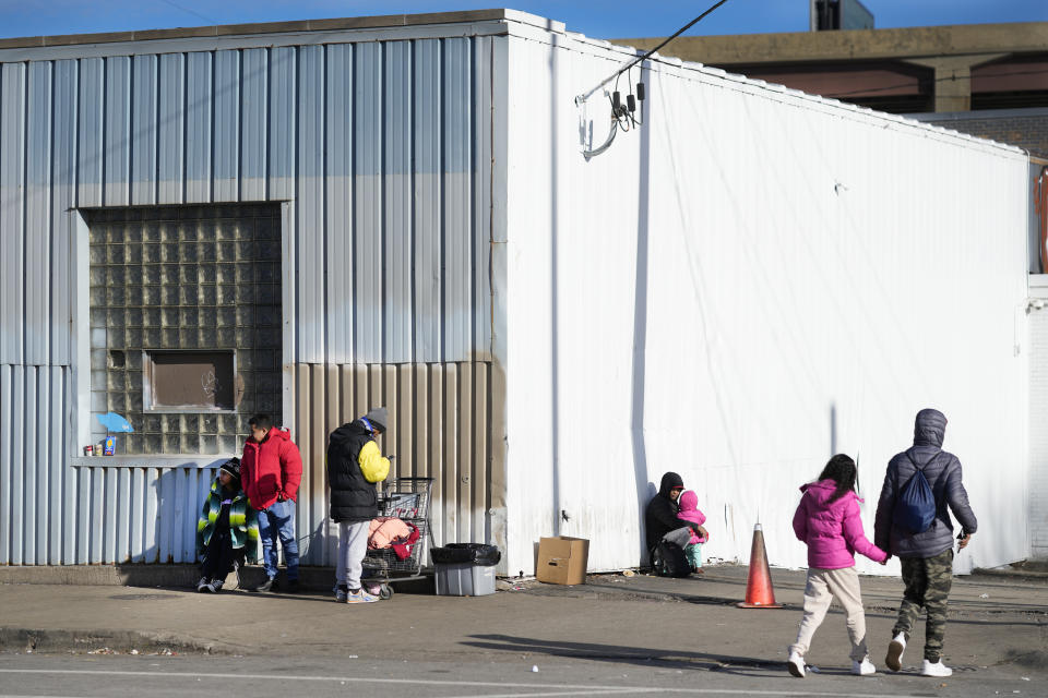 Immigrants stand outside and return to a shelter in the Pilsen neighborhood of Chicago, Tuesday, Dec. 19, 2023. The death of a 5-year-old migrant boy and reported illnesses in other children living at the shelter has raised concerns about the living conditions and medical care provided for asylum-seekers arriving in Chicago. Four more people living in the same shelter — mostly children — were hospitalized with fevers this week. (AP Photo/Charles Rex Arbogast)