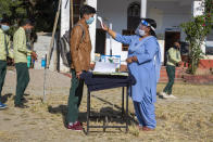 A staff member tests the temperature of students before allowing them into classrooms, as a precautionary measure against the coronavirus, at the Government Senior Secondary School in Dari, near Dharmsala, India, Friday, Nov. 6, 2020. (AP Photo/Ashwini Bhatia)