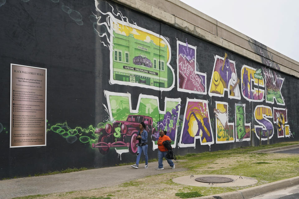 Javohn Perry, left, of Seattle, and her cousin, Danielle Johnson, right, of Beggs, Okla., walk past a mural commemorating Black Wall Street in Tulsa, Okla., on Monday, April 12, 2021. (AP Photo/Sue Ogrocki)