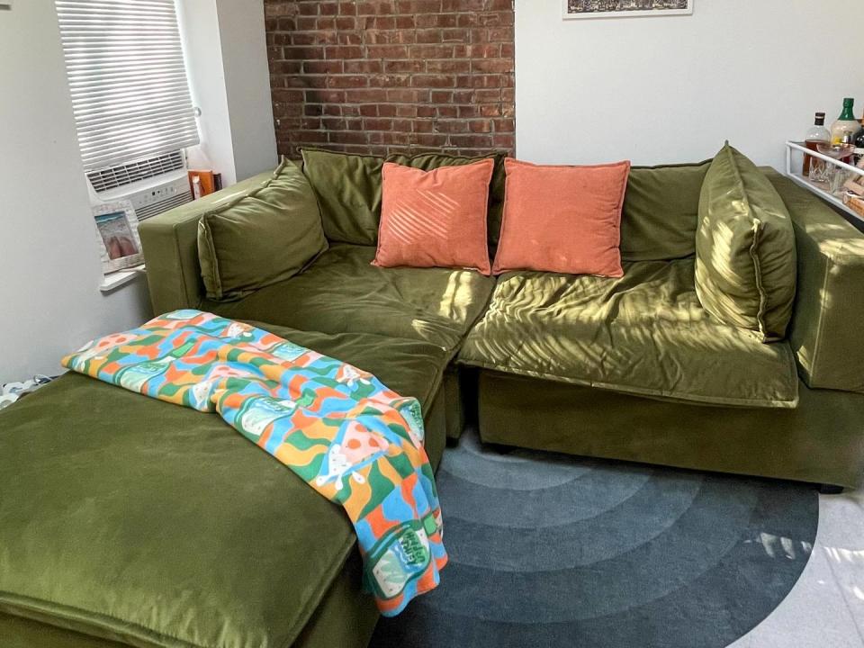 green velvet sofa and ottoman with orange pillows and colorful throw blanket