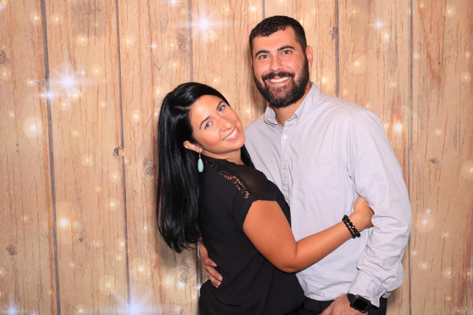 Amanda Irizarry and her husband, Bryan Bates, pose for a photo in front of the popular gold sparkle backdrop at The Shutter Bird Photo Booth.