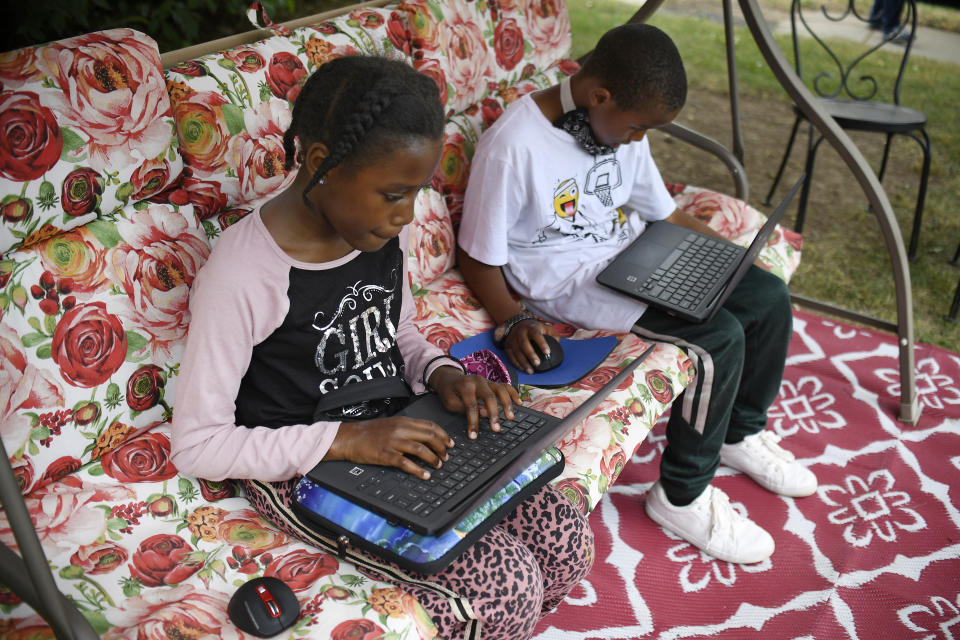 In this Friday, June 5, 2020 photo, Fourth-grader Sammiayah Thompson, left, and her brother third-grader Nehemiah Thompson work outside in their yard on laptops provided by their school system for distant learning in Hartford, Conn. With huge percentages of students unplugged from distance learning, educators at schools around the country have been working to understand why. (AP Photo/Jessica Hill)