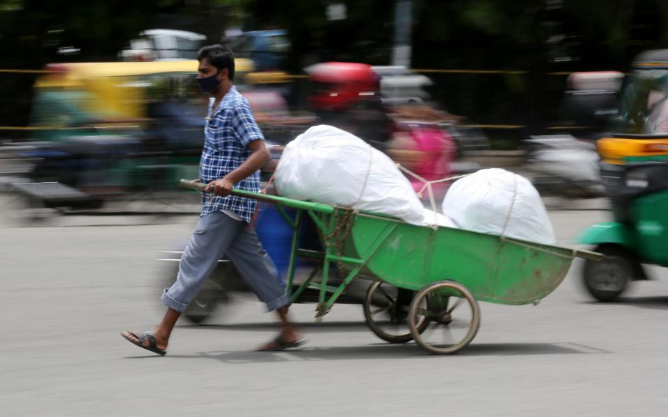 An Indian man pulling hand cart in a busy market area, during an extended lockdown over suspected coronavirus disease (COVID-19) cases in Bangalore, India - Shutterstock