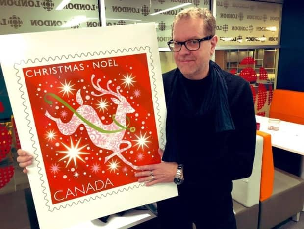 Many of Lewis's usual creations for Canada Post grace the upper-right corners of envelopes across the country. In this photo, taken in November 2019, he holds up one of his designs for Canada Post's Christmas collection.