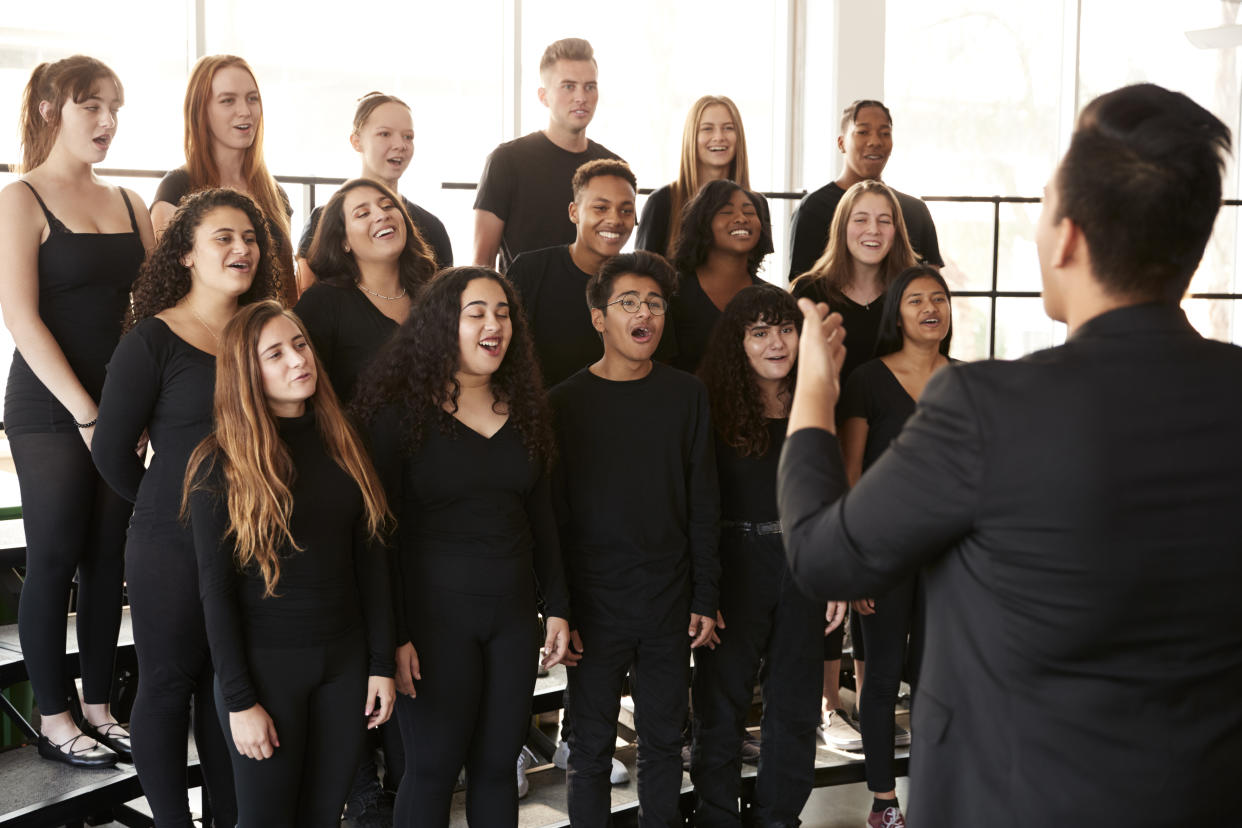 Male And Female Students Singing In Choir With Teacher At Performing Arts School