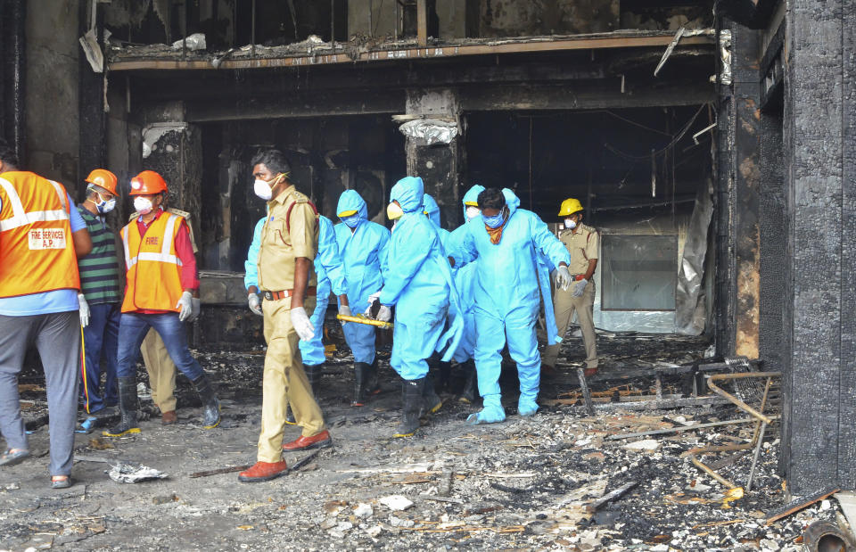 Rescuers in protective suits carry the body of a victim from Hotel Swarna Palace where a fire broke out early morning in Vijayawada, Andhra Pradesh state, India, Sunday, Aug. 9, 2020. The fire in the hotel being used as a COVID-19 facility killed seven coronavirus patients. (AP Photo)
