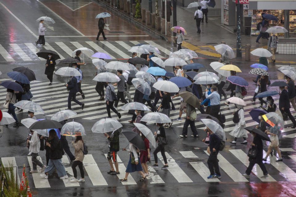 Commuters with umbrellas walk a crosswalk as Typhoon Mindulle travels off the coast of Japan Friday, Oct. 1, 2021, in Tokyo. Japan fully came out of a coronavirus state of emergency for the first time in more than six months as the country starts to gradually ease virus measures to help rejuvenate the pandemic-hit economy as the infections slowed. (AP Photo/Kiichiro Sato)