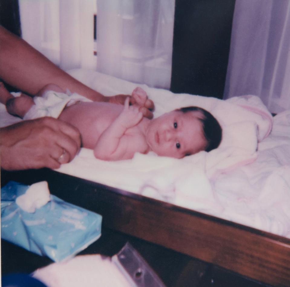 Infant lying on a changing table with an adult's hands gently securing the baby