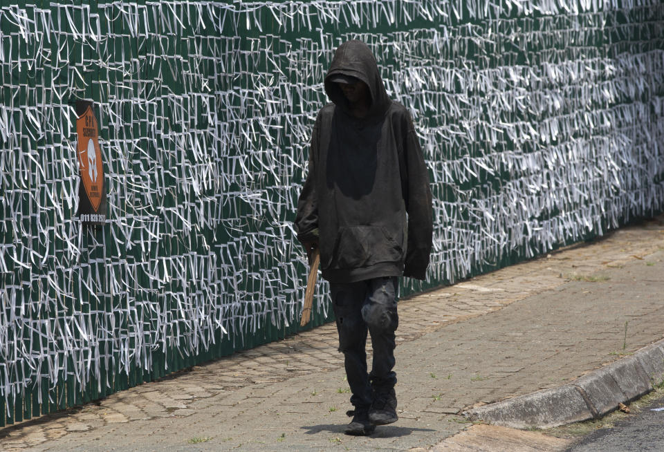 FILE - In this Jan. 20, 2021, file photo, a pedestrian passes the perimeter fence of the Presbyterian Church where ribbons represent some of the people who have died in the COVID-19 pandemic, in Bedfordview, Johannesburg, South Africa. Africa has surpassed 100,000 confirmed deaths from COVID-19 as the continent praised for its early response to the pandemic now struggles with a dangerous resurgence and medical oxygen often runs desperately short. (AP Photo/Denis Farrell, File)