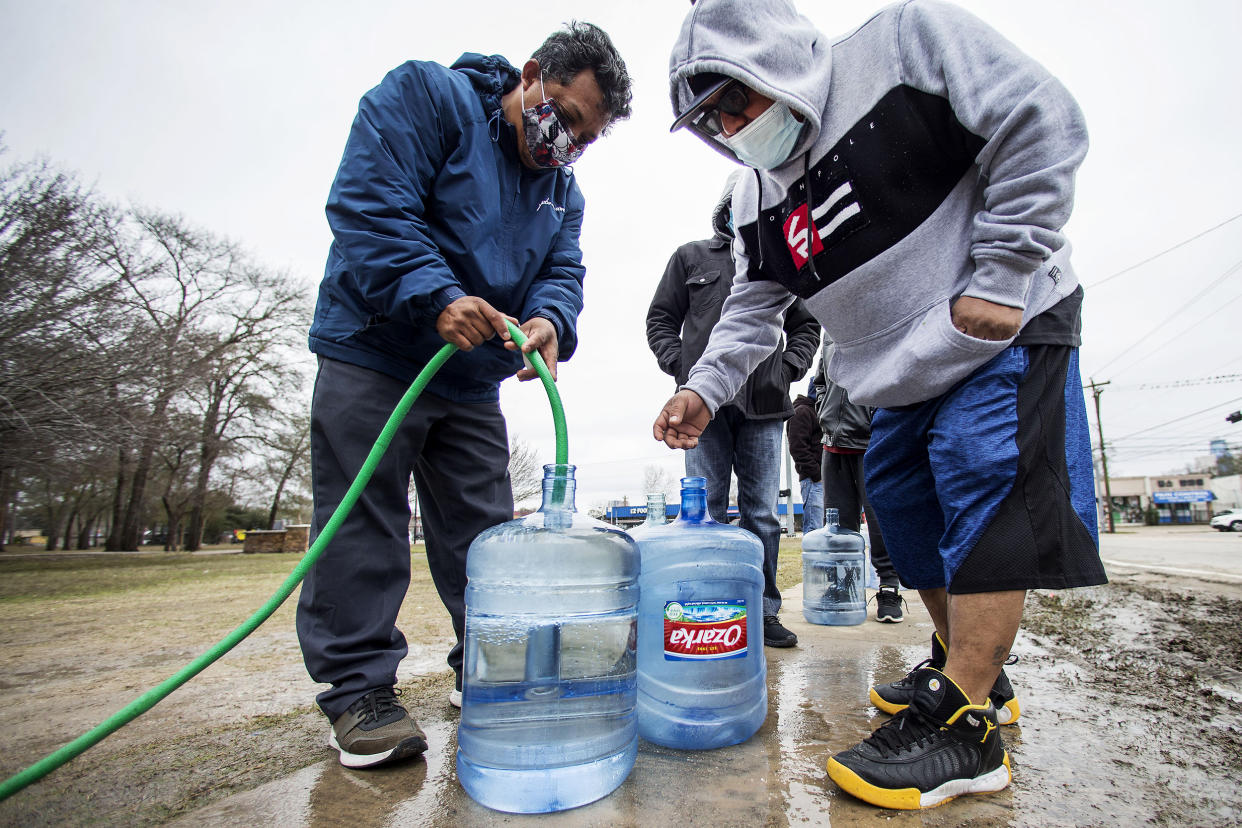 Image: Victor Hernandez, left, and Luis Martinez fill their water containers with a hose from a spigot in Haden Park (Brett Coomer / Houston Chronicle via AP)