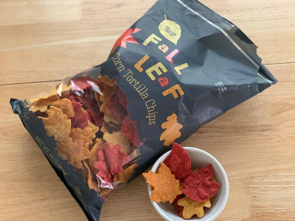 Black bag of Trader Joe's fall leaf tortilla chips alongside leaf-shaped chips in a small white bowl on a wooden table