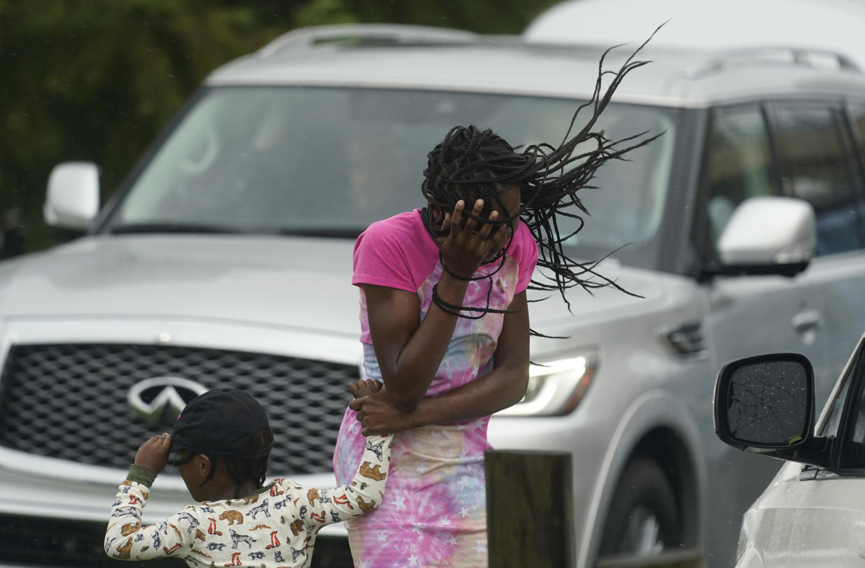 A woman and child stand near cars as they block their faces from the wind and rain.