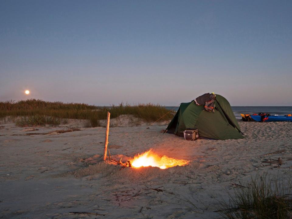 A full moon rises over a tent next to a campfire on Capers Island, Charleston SC.