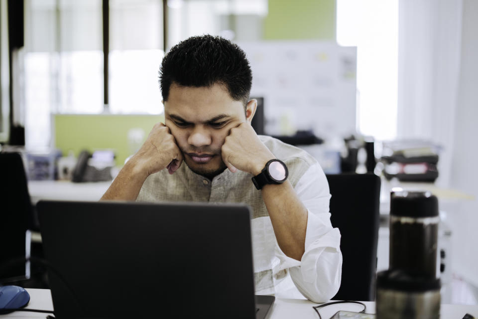 Person in front of a laptop with hands on temples, appearing stressed or concentrated