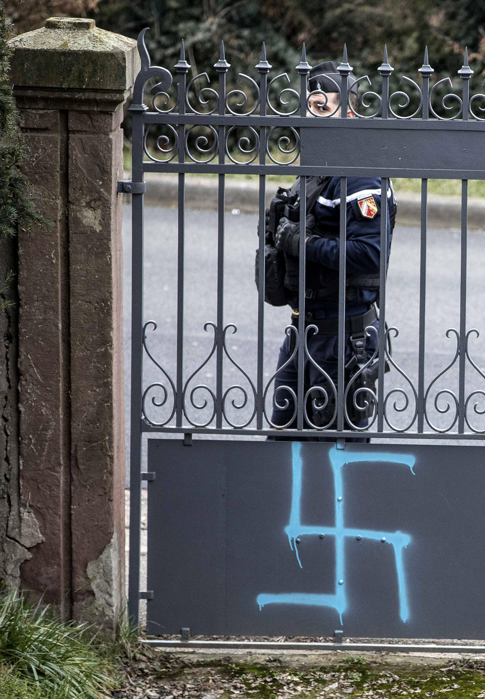 A gendarme guards the Jewish cemetery where the gate and tombs were tagged swastikas are pictured in the Jewish cemetery of Quatzenheim, eastern France, Tuesday, Feb.19, 2019. Marches and gatherings against anti-Semitism are taking place across France following a series of anti-Semitic acts that shocked the country. (AP Photo/Jean-Francois Badias)