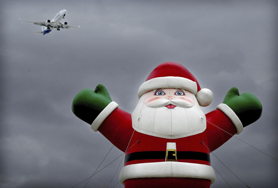 An Alaska Airlines flight from Seattle makes its final approach into Ontario International Airport as it flies over an inflatable Santa Claus atop a car dealership under dark skies in Ontario, Calif., on Tuesday, Dec. 19, 2023. (Will Lester/The Orange County Register via AP)