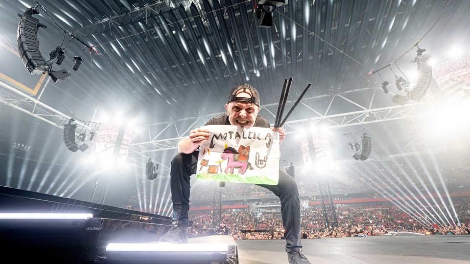 Lars Ulrich onstage holding a handmade Metallica sign