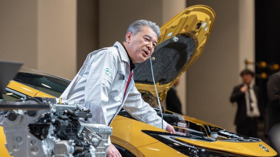 a man in a white jacket with a yellow car behind him