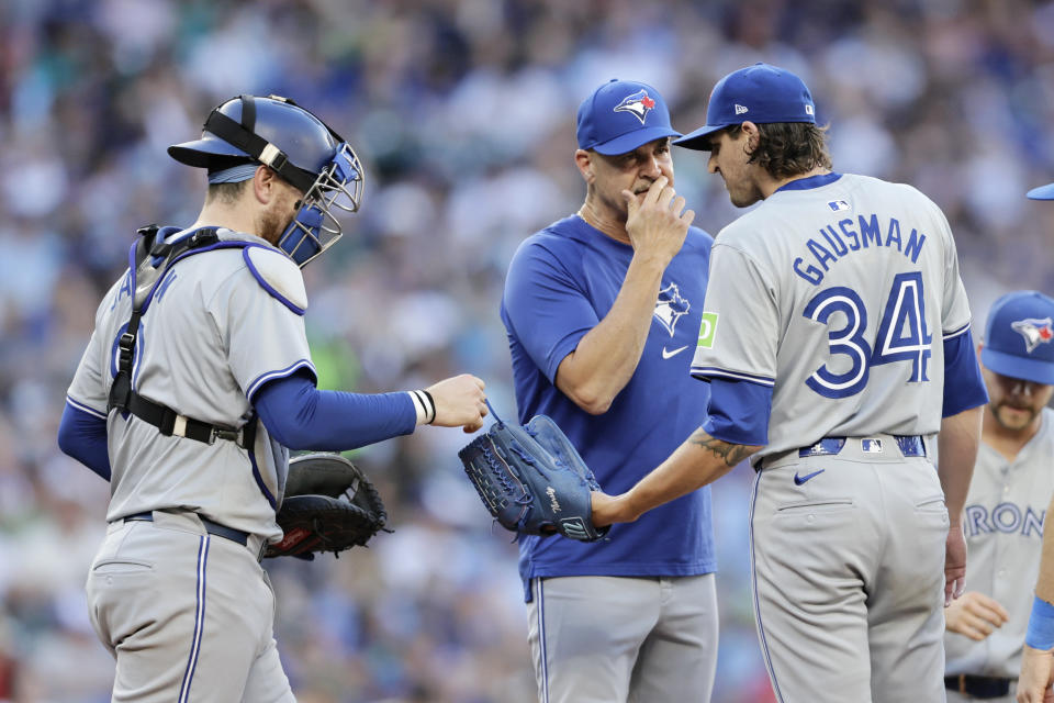 Toronto Blue Jays catcher Danny Jansen, left, hands starting pitcher Kevin Gausman (34) the ball as they have a conference on the mound with pitching coach Pete Walker, seocnd from left, during the fourth inning of a baseball game against the Seattle Mariners, Friday, July 5, 2024, in Seattle. (AP Photo/John Froschauer)