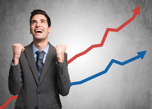 A businessman cheers as he watches a chart of rising returns.