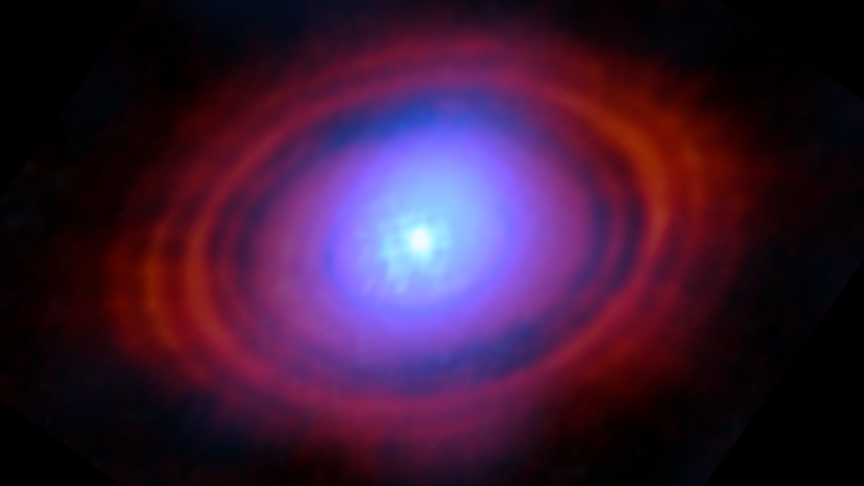  A slightly blurry blue orb in the center of the image is surrounded by a gradient disk of purple, and then red, hazes. The structure is seen against a black background. 