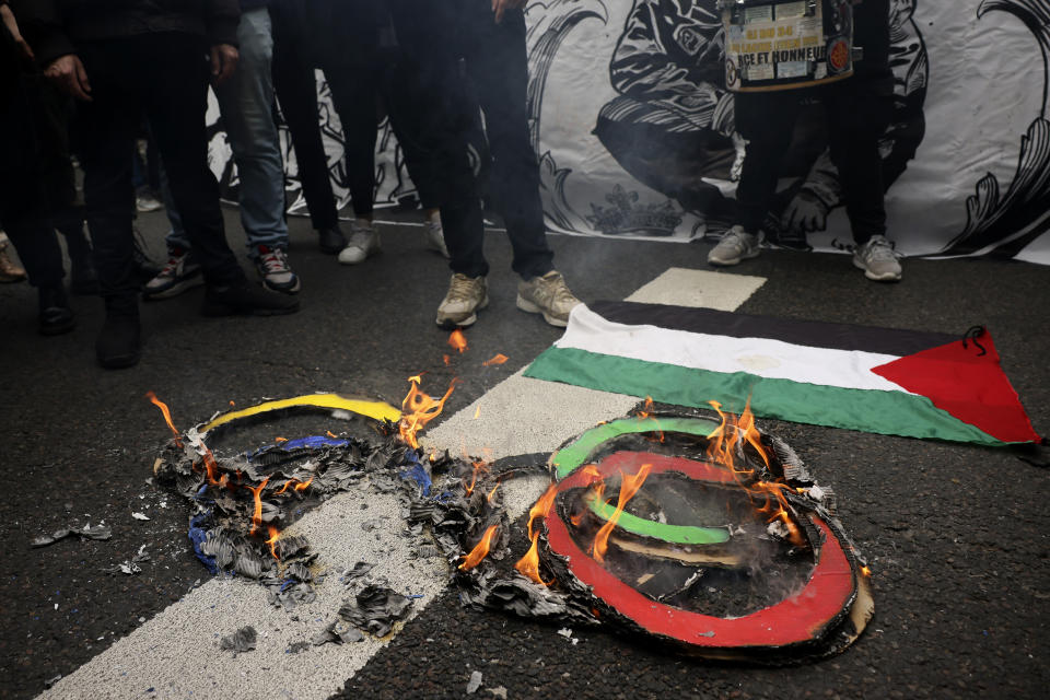 Protesters burn olympic rings on the pavement near a Palestinian flag during the May Day demonstration, Wednesday, May 1, 2024 in Paris. (AP Photo/Thomas Padilla)