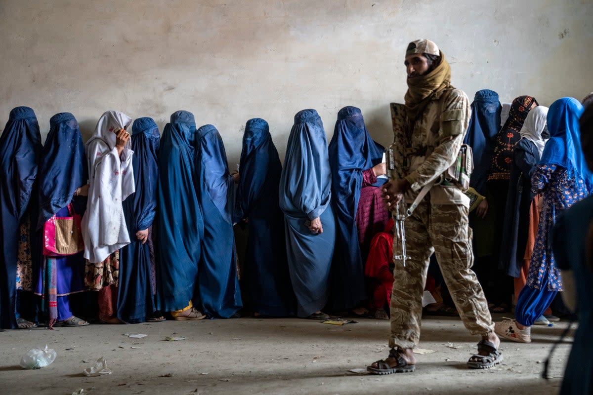 A Taliban fighter stands guard as women wait to receive food rations distributed by a humanitarian aid group, in Kabul, Afghanistan (AP)