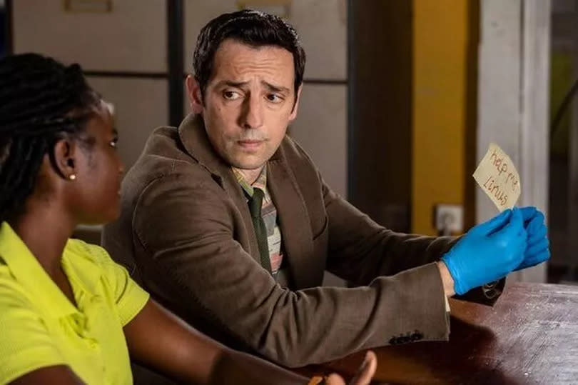 Ralf Little in character on Death in Paradise, wearing blue gloves