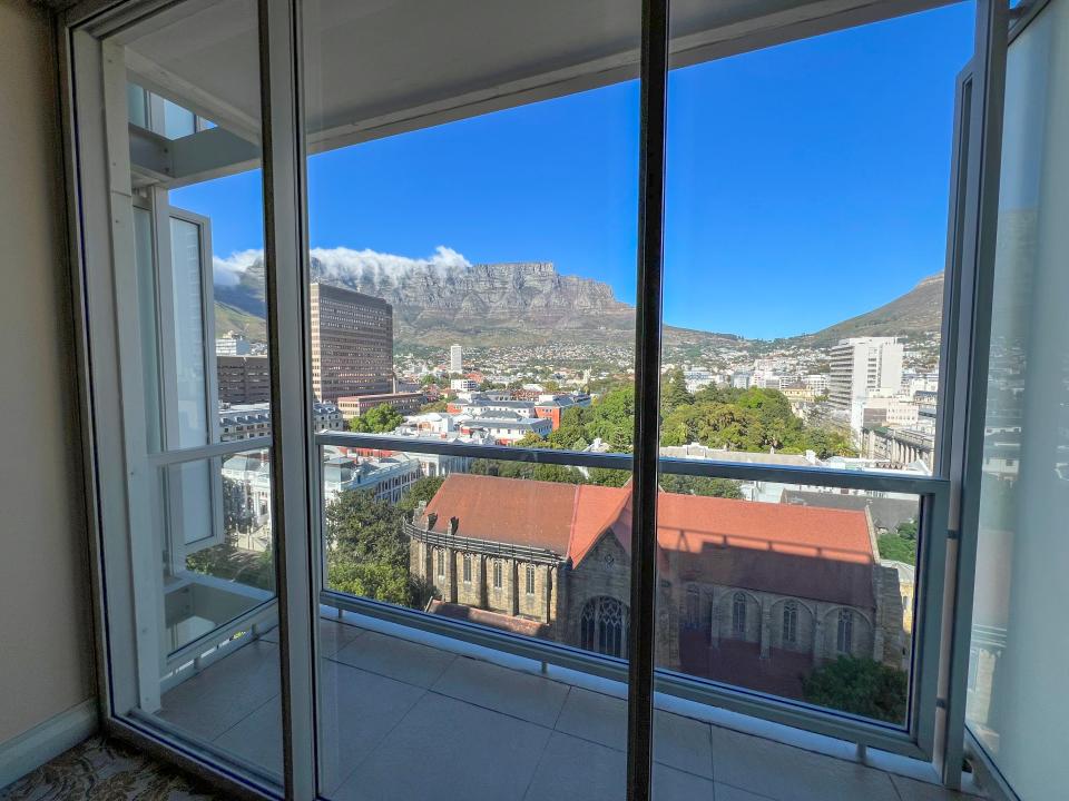A view from a hotel window with a view of Cape Town, South Africa. There is a view of buildings with brown rooves, skyscrapers, and mountains