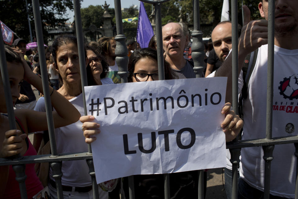 FILE - In this Sept. 3, 2018 file photo, students and National Museum employees protest outside the institution after it was gutted by an overnight fire in Rio de Janeiro, Brazil. The sign reads in Portuguese: "Patrimony. In Mourning." Among the objects feared lost from the 20 million-piece collection: furniture and art belonging to the royal family; recordings of indigenous languages, some of which are no longer spoken; priceless specimens of everything from rare butterflies and other insects to coral; a collection of Egyptian mummies and artifacts considered the largest in Latin America; frescoes from Pompeii and one of the oldest human fossils ever found in the Americas.(AP Photo/Silvia Izquierdo, File)