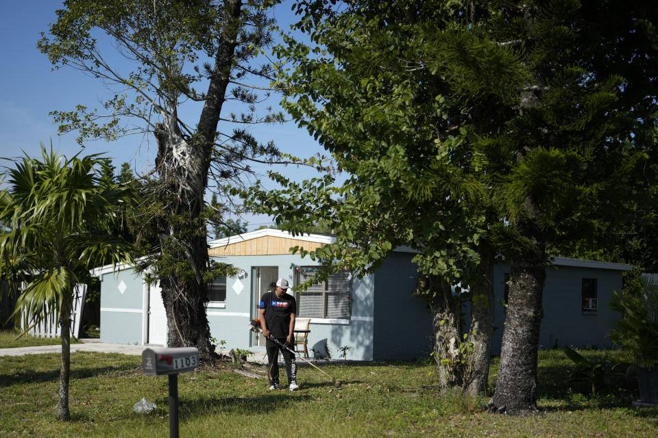 Alexis Llanos, 27, trims the lawn of the home the Llanos family moved into in October 2023, five years after fleeing Venezuela to Colombia to escape death threats and political persecution, in Lehigh Acres, Fla., Dec. 27, 2023. The family is among the first migrants allowed into the U.S. under the Biden administration's new "safe mobility offices," intended to streamline the U.S. refugee process so migrants don't give up and pay smugglers to make the journey north. (AP Photo/Rebecca Blackwell)