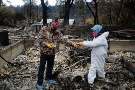 Vanthy Bizzle hands some small religious figurines to her husband Brett Bizzle in the remains of their home after returning for the first time since the Camp Fire forced them to evacuate in Paradise, California, U.S. November 22, 2018. REUTERS/Elijah Nouvelage
