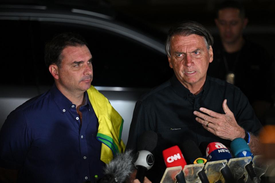 Brazilian President and re-election candidate Jair Bolsonaro (R) speaks to the press after learning the results of the legislative and presidential election next to his son Flavio Bolsonaro (L) in Brasilia, on October 2, 2022. - Brazil's bitterly divisive presidential election will go to a runoff on October 30, electoral authorities said Sunday, as incumbent Jair Bolsonaro beat expectations to finish a relatively close second to front-runner Luiz Inacio Lula da Silva. Lula, the veteran leftist seeking a presidential comeback, had 48.1 percent of the vote to 43.5 percent for the far-right President, with 98 percent of polling stations reporting, according to official from the Superior Electoral Tribunal. (Photo by EVARISTO SA / AFP) (Photo by EVARISTO SA/AFP via Getty Images)