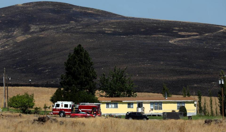 A fire truck stages next to a home that was threatened by a two-alarm wildfire that forced people from homes Monday afternoon just north of Benton City. There were no immediate details on the size or cause of the blaze.