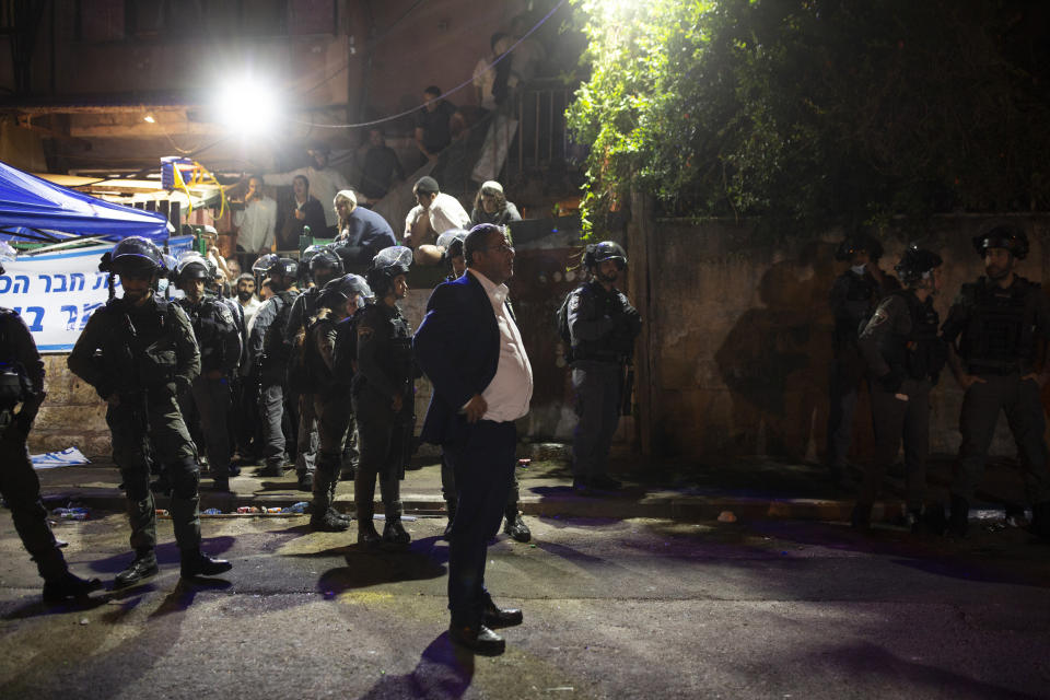 Itamar Ben-Gvir, the leader of a far-right party, stands with police guarding a Palestinian home occupied by Israeli settlers, at a protest against the forcible eviction of Palestinian families from their homes in the Sheikh Jarrah neighborhood of Jerusalem, Thursday, May 6, 2021. Palestinians and Israeli settlers hurled rocks and chairs at each other in Sheikh Jarrah, where dozens of Palestinians are at risk of being evicted following a long legal battle with Jewish settlers trying to acquire property in the neighborhood, which is just north of Jerusalem's Old City. (AP Photo/Maya Alleruzzo)