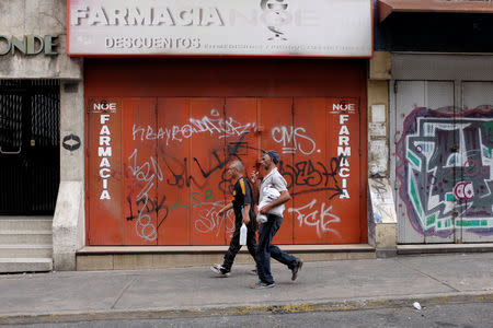 People walk in front of a closed drugstore in downtown Caracas, Venezuela August 18, 2018. REUTERS/Marco Bello