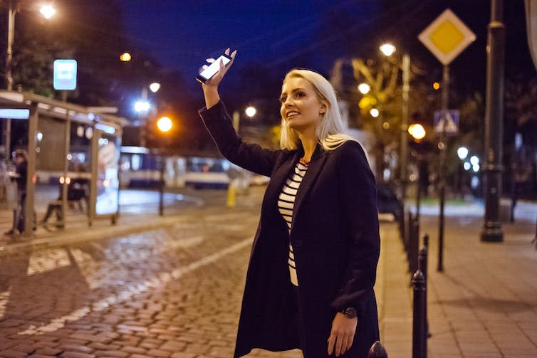 Una mujer joven sostiene un teléfono inteligente en la mano y llama a un taxi