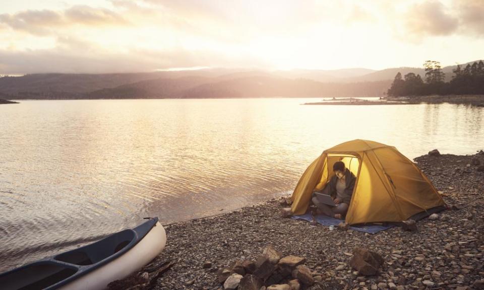 He has the best office in the worldShot of a young man using a laptop while camping on a remote inlet in Tasmania