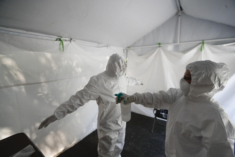 A healthcare worker disinfects a colleague at the end of a day of collecting sample to test for the new coronavirus inside a mobile diagnostic tent, in the Coyoacan district of Mexico City, Friday, Nov. 13, 2020. Mexico City announced Friday it will order bars closed for two weeks after the number of people hospitalized for COVID-19 rose to levels not seen since August. (AP Photo/Eduardo Verdugo)