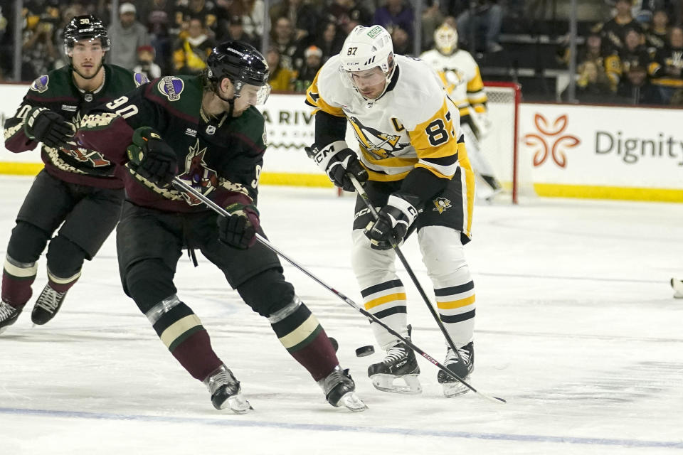 Arizona Coyotes' J.J. Moser (90) and Pittsburgh Penguins' Sidney Crosby (87) battle for the puck during the second period of an NHL hockey game Monday, Jan. 22, 2024, in Tempe, Ariz. (AP Photo/Darryl Webb)